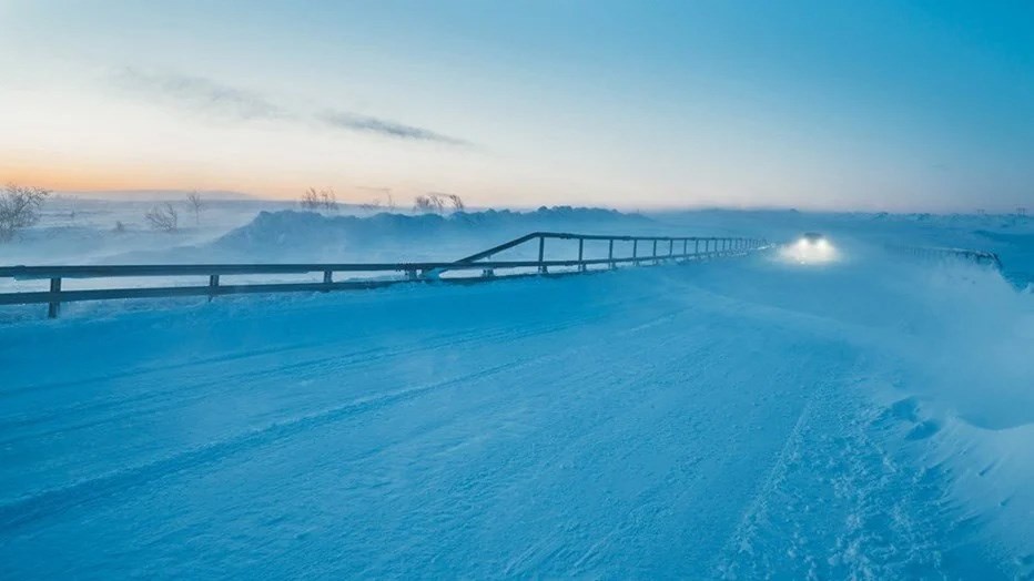 I Flatruet ligger Sveriges högst belägna allmänna väg. Den förenar Funäsdalen med Ljungdalen och slingrar sig genom fjällkedjan längs den norska gränsen. Här, 975 meter över havet, har Skanska byggt broarna över Kojebäcken, Rutjärnsbäcken och Skärkan.  Vintreig väg med snö som yr. Broräcke med bild som skymtas i snöröken.