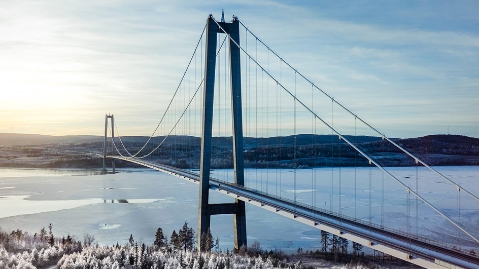 Högakustenbron i vinterlandskap med isigt vatten under. Högakustenbron är utformad för att ha så liten påverkan som möjligt på denna unika miljö och den är på samma gång dramatisk och elegant där den glider fram genom landskapet.