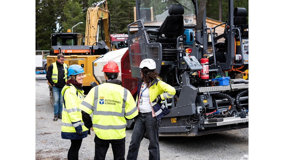 Tre personer i varselkläder står på en byggarbetsplats och pratar.