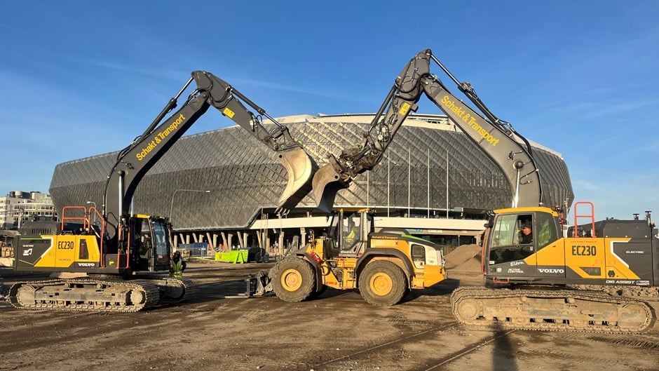 Tre gula elmaskiner, två bandgrävare coh en hjulgrävare poserar med Tele2s arenabyggnad i bakgrunden.