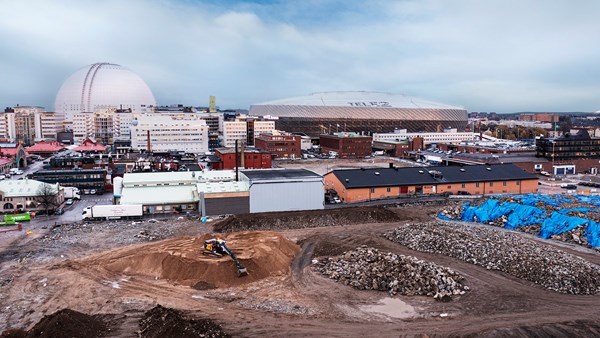 Elektisk grävmaskin på stor jordyta, i bakgrunden syns kupolen på Globen.